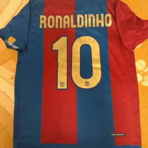 Barcelona Ronaldinho #10 Nike fotbollströja - Klassisk FC Barcelona fotbollströja med Ronaldinho och nummer 10 på ryggen. Tröjan är randig i blått och rött, har klubbmärke och Nike-logga på bröstet samt katalanska flaggan på ärmen. Tillverkad i lätt och ventilerande material.