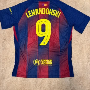 FC Barcelona Lewandowski matchtröja Nike L - Barça matchtröja med Lewandowski 9 på ryggen, officiell Nike Dri-FIT ADV. Klassiska blå och röda ränder, gula detaljer och klubbmärke på bröstet. Spotify-logga framtill, UNHCR-tryck bak. Lätt och ventilerande material perfekt för fotboll.