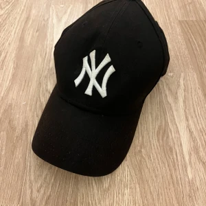 Svart New York Yankees keps 9FORTY - Snygg svart keps från New Era med klassiskt New York Yankees-logo broderat i vitt framtill. Modellen är 9FORTY och har justerbar rem baktill. Perfekt för dig som vill ha en sportig och urban look. Materialet är bomull och kepsen är officiell MLB-merch.