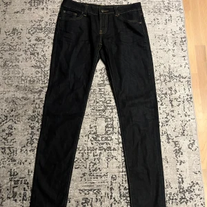 Mörkblå skinny jeans från Nudie - Snygga mörkblå jeans från Nudie med klassisk gul kontrastsöm och ikonisk broderad bakficka. Modellen är skinny fit med normal midja och tillverkad i stretchig bomullsdenim för en bekväm passform. Perfekta för dig som gillar stilrena och tidlösa jeans. Midjan är sydd så att det passar 31 men igenkligen 32/33, Thin Finn 