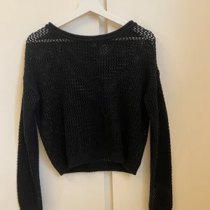Svart stickad tröja med hål - Svart stickad tröja med stora hål och långärmad design. Tröjan har en rundad hals och är lite loose i passformen, perfekt för lager-på-lager elever en dag på stranden. Materialet är stickat och ger en cool, luftig känsla. Enkel att styla med jeans eller kjol för en chill look.