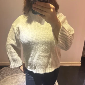 Vit stickad polotröja i loose fit - Säljer en vit stickad polotröja med ribbad hög krage och breda långärmar. Tröjan har en loose fit och är tillverkad i mjukt material som passar perfekt när det är kallt. Enkel och clean design som är lätt att matcha med jeans eller kjol.