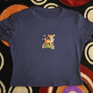 Blå croppad t-shirt med Bambi-tryck - Snygg blå croppad t-shirt med ett gulligt Bambi-tryck framtill. T-shirten har rund hals och korta ärmar. Materialet känns mjukt och skönt, perfekt för dig som gillar söta motiv och vill ha en chill stil.