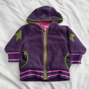 Lila teddyjacka - Lila teddyjacka från Lindex i storlek 74. Har huva, gröna och rosa detaljer samt stjärnor på ärmarna. Fraktar inom 24h!
