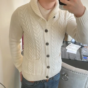Vit stickad cardigan med mönster - Snygg vit stickad cardigan med mönster. Perfekt att slänga på sig när det är lite kyligt ute. Modellen är 180cm, 73kg. Priset går att diskutera så skicka gärna iväg ett prisförslag!