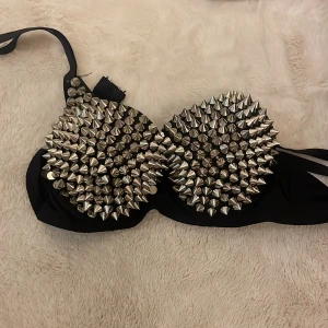 Svart tubtopp med silvernitar - Säljer en svart tubtopp med massor av silverfärgade konformade nitar över hela framsidan. Toppen är axelbandslös och har en edgy, statement look som verkligen sticker ut. Perfekt för dig som vill ha något unikt och vågat till nästa fest!