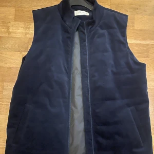 Mörkblå quiltad manchesterväst Sayless - Snygg mörkblå väst från Sayless i quiltad manchester med dragkedja framtill och två sidofickor. Insidan är fodrad i grått syntetmaterial. Perfekt för lager-på-lager och chill stil. Enkel, stilren design med hög krage.