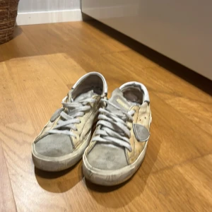 Philippe Model beige sneakers med grå detaljer - Snygga sneakers från Philippe Model i beige och grått med vita snören och vit hälkappa. Skorna har en klassisk låg profil, rund tå och platt sula. Materialmix av skinn och mocka med den ikoniska skölden på sidan. Perfekta för en avslappnad och trendig look.