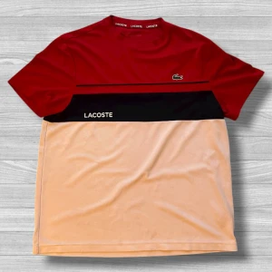 Röd, svart och beige Lacoste t-shirt - Snygg t-shirt från Lacoste Sport i färgblock med rött upptill, svart mittparti och beige nedtill. Klassisk krokodillogga på bröstet och Lacoste-tryck på magen. Skön passform och tillverkad i mjukt material, perfekt för en sportig look.