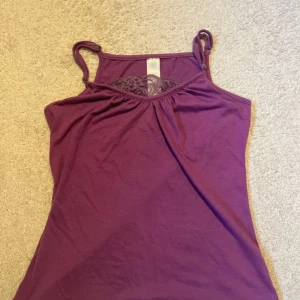 spets linne - Säljer en lila linnetopp med smala axelband och snygg spetsdetalj framtill vid halsen. Toppen har en mjuk och skön känsla, perfekt för varma dagar. Enkel och stilren design som är lätt att matcha med jeans eller shorts.