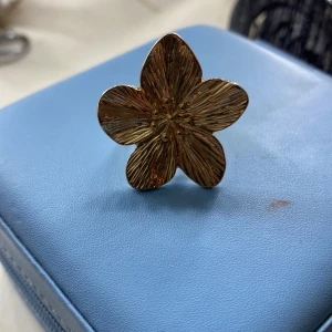 Stor guldfärgad blomring - Statementring i guldfärg med en stor, detaljerad blomma som motiv. Ringen har en bred, justerbar ringbas och blomman har tydliga ådror för en cool 3D-effekt. Perfekt accessoar för dig som vill sticka ut med något unikt och trendigt.