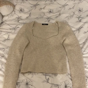 Beige ribbstickad tröja med fyrkantig ringning - Superfin beige ribbstickad tröja från Gina Tricot med lång ärm och snygg fyrkantig ringning. Tröjan har en croppad passform och diskret mönsterdetalj framtill. Perfekt att styla med jeans eller kjol för en trendig look.