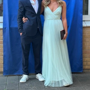 Balklänning - Superfin ljusblå långklänning med v-ringad omlott framtill och tunna axelband. Klänningen har plisserad kjol och öppen detalj i ryggen. Perfekt för student eller bal! Materialet känns lätt och flowy.