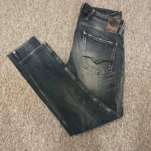 Replay jeans Anbass  - Snygga Replay Anbass jeans i mörkblå tvätt med slitningar och lätt distressed look. Klassisk femficksmodell med raka ben och detaljerade bakfickor. Jeansen är tillverkade i bomull och har en bekväm passform som passar till många stilar. Storlek 32/34