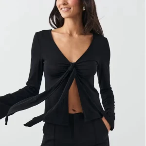 Svart omlottopp med knyt framtill - Svart långärmad topp med djup v-ringning och knyt framtill som skapar en snygg omlott-effekt. Toppen är croppad och har en öppen detalj vid magen. Perfekt för dig som gillar trendiga och stilrena plagg med lite edge.