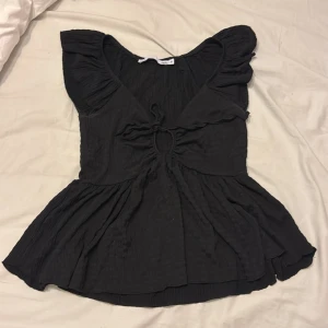 Svart blus med volang och knyt - Säljer en svart blus från 157 med volangdetaljer vid axlarna och ett snyggt knyt framtill som skapar en liten öppning. Blusen har en v-ringad hals och är kortärmad med en luftig, lätt rynkad nederdel. Perfekt för dig som gillar en feminin och trendig look.