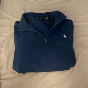 Blå half zip tröja från Polo Ralph Lauren - Snygg blå långärmad tröja från Polo Ralph Lauren med half zip och klassisk krage. Riktigt skönt material, nästan aldrig använd då den är lite stor. Skick 9,5/10 .De bara fråga om mer bilder. Självklart äkta. Hör av dig vid minsta fundering!