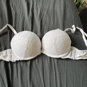 Vit spetsblus Linnea från Lindex - Säljer en vit bh från Lindex, modell Linnea, med vacker spets och blommigt mönster på kuporna