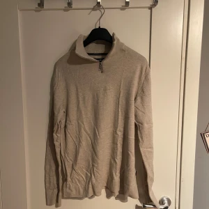 Beige halvzip tröja från Jack & Jones - Beige långärmad tröja från Jack & Jones med halv dragkedja vid kragen. Tröjan är i mjukt material och har ribbade muddar vid ärmslut och nederkant. Perfekt för lager-på-lager under höst och vinter. Den är i stl L men passar som S