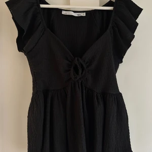 Svart kort topp med volangärm - Svart kort topp från lager 157 med volangärmar och knytdetalj framtill. Toppen har en lätt rynkad struktur och v-ringad hals. Perfekt för dig som gillar en feminin och trendig look. Materialet känns mjukt och luftigt.