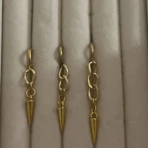 Guldiga örhängen med kedjor och spets - Säljer örhängen i guld i tre olika storlekar med kedjelänkar och spetsiga hängen. Designen är edgy och modern, perfekt för dig som gillar statement-smycken. Kedjorna har olika former och ger en unik look. Passar dig som vill sticka ut med dina accessoarer. Säljs som par