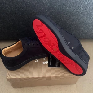 Christian Louboutin  skor  - Snygga mörkblåa  sneakers från Christian Louboutin i mocka med klassisk röd sula och diskret logga på sidan. Skorna har rund tå, snörning och platt sula. Perfekta för dig som vill ha en lyxig och stilren look med en touch av Paris.