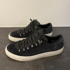 Svarta mockasneakers från Diemme - Snygga svarta sneakers från Diemme i mocka med vit platt sula. Skorna har coola metallöglor och snörning som ger en unik look. Perfekta för dig som gillar stilrena men ändå lite sportiga skor. Tillverkade i Italien och riktigt bekväma.