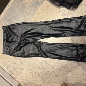 Svarta skinnbyxor från Calzedonia - Snygga svarta byxor i skinnimitation från Calzedonia. Byxorna har raka ben, två bakfickor och bälteshällor. Perfekta för dig som vill ha en edgy look med stilren känsla. Materialet är mjukt och följsamt syntetskinn.