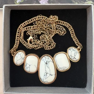 Guldigt halsband med marmorinspirerade stenar - Unikt halsband med tjock guldfärgad kedja och fem vita stenar med svarta marmormönster. Stenarna är infattade i guldfärgade ramar och har olika organiska former som ger ett coolt statement. Perfekt för dig som gillar att sticka ut med accessoarer.