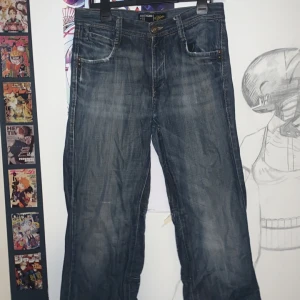 Blå jeans från SMOG supercoola nitar studs lågmidjat - Säljer ett par blå jeans från SMOG med snygg tvätt och slitningar. Det finns tecken på användning vid fickorna, och vid benöppningarna. 