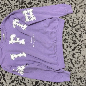 Lila sweatshirt med tryck från H&M - Cool lila sweatshirt från H&M med stora vita bokstäver och texten 'Avenue New York City' på framsidan. Tröjan har långärmad passform och är gjord i mjuk bomull. Perfekt för dig som gillar streetstyle och vill sticka ut med färg.