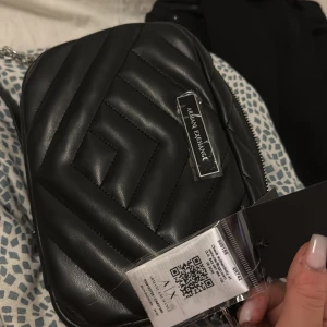 Svart quiltad axelväska Armani Exchange - Helt ny Svart axelväska från Armani Exchange med quiltad design och silverfärgad kedja. Väskan har en snygg geometrisk sömnad, dragkedja upptill och logotyp framtill. Insidan är fodrad med mönstrat tyg och har en liten ficka. Perfekt storlek för det viktigaste. aldrig använt!