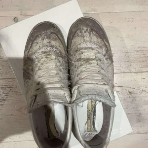 sneakers i distressed stil - Unika sneakers vit och grå färg med distressed och smutsad look. Skorna har snörning, rund tå och platt sula. Tillverkade i skinn och textil för en edgy vibe. Perfekta för dig som gillar statement pieces och streetwear.