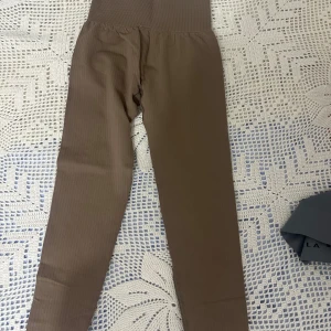 Bruna tränings leggings från ICANIWILL - Säljer ett par bruna ribbade leggings från ICANIWILL i storlek XS. De har hög midja och är tillverkade i stretchigt material med 92% nylon och 8% spandex. Perfekta för träning och har en snygg, tight passform med diskret logga på höften.