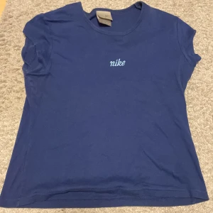Mörkblå Nike t-shirt i bomull - En retro Nike tröja, mörkblå t-shirt från Nike med broderad logga framtill. Klassisk rund halsringning och korta ärmar. Tillverkad i mjuk bomull, perfekt för en sportig och avslappnad stil.