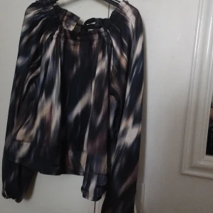 Mönstrad blus med knyt från H&M XS - Säljer en luftig blus från H&M i storlek XS. Blusen har ett abstrakt mönster i svart, beige, grönt och grått, långa ärmar och en snygg knytning vid halsen. Tillverkad i ett lätt, glansigt material som ger en cool vibe.
