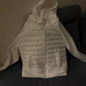 Vit quiltad pufferjacka med huva - Säljer en fräsch vit pufferjacka med huva och dragkedja framtill. Jackan har quiltad framsida och två fickor med dragkedja. Perfekt för dig som gillar stilren och enkel design. Passar till chill dagar och när du vill hålla dig varm. S/M storlek 