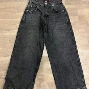 Svarta wide jeans från BDG - Säljer ett par svarta jeans från BDG med breda ben och hög midja. Klassisk femficksmodell med stora bakfickor och knappstängning. Jeansen har en cool, mörk tvätt och är tillverkade i robust denim. Perfekt för dig som gillar loose fit och streetstil. Byxorna har röd stitching runt midjan. Säljer för 150kr vid bra skick med lite slit längst ned.