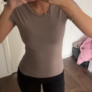 Beige tight t-shirt med rund hals - Säljer en enkel och stilren beige t-shirt med rund hals. Modellen är tight och har korta ärmar, perfekt för dig som gillar en clean och minimalistisk look. Materialet känns mjukt och stretchigt mot kroppen. Ginas soft touch kollektion!