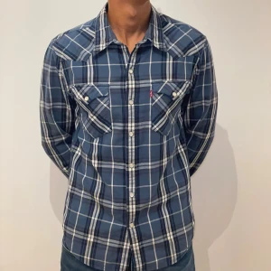 Levi's Blå rutig skjorta  - Väldigt Snygg blå rutig skjorta från Levi's med klassisk westernkrage och vita knappar. Skjortan har två bröstfickor med lock och knapp, samt en liten röd Levi's-tag på ena fickan. Långärmad och tillverkad i mjuk bomull. Perfekt för dig som gillar avslappnad stil. Pris kan diskuteras