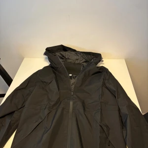 Svart vindjacka med huva - Säljer en svart vindjacka med huva och dragkedja framtill. Jackan har en clean look, elastiska muddar vid ärmsluten och praktiska fickor med dragkedja. Perfekt för blåsiga dagar och enkel att matcha med allt. Snygg och funktionell för dig som gillar stilren design. Helt ny. Jag är 175 o väger 75