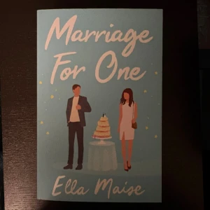 Marriage For One - En charmig bok med en modern, romantisk känsla. Omslaget visar två personer vid en bröllopstårta, vilket hintar om relationer och oväntade möten. Perfekt för dig som gillar kärlekshistorier med en twist.
