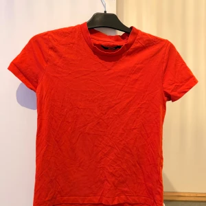 Röd t-shirt från Bik Bok - En enkel och stilren orange t-shirt från Bik Bok i storlek S. T-shirten har rund halsringning och korta ärmar, perfekt till jeans eller kjol. Tillverkad i mjuk bomull för en skön känsla hela dagen.