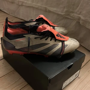 Adidas Predator Elite FT FG fotbollsskor - Säljer ett par Adidas Predator Elite FT FG fotbollsskor i metallicgrå och röd med svarta detaljer. Skorna har snörning, låg profil och mönstrad sula för bästa grepp på planen. Ovandelen är i syntetmaterial och insidan är röd med svart text. Perfekta för dig som vill sticka ut på fotbollsplanen. Pris går att diskutera 
