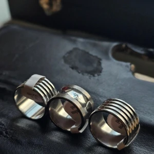 Tre breda silverringar storlek 18 - Säljer tre coola breda ringar i silverfärgat metall, storlek 18. Två av ringarna har ett randigt mönster med flera parallella linjer runt om, medan den tredje är helt slät och blank. Alla är I Rostfritt och ca 18 mm
