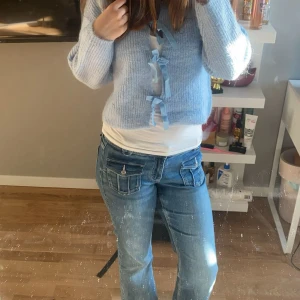 Ljusblå kofta med rosetter - Superfin ljusblå kofta i stickat material med söta rosetter framtill. Koftan har rund halsringning och långa ärmar, perfekt för lager-på-lager. Mysig och trendig att styla till jeans eller kjol.Man kan ha utan linne också men jag valde att ha ett vitt linne under.