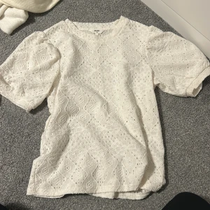 Vit spetsblus från Object - Superfin vit blus från Object med puffiga korta ärmar och vackert broderat spetsmönster. Blusen har rund halsringning och är tillverkad i bomull, vilket gör den både luftig och bekväm. Perfekt att styla med jeans eller kjol för en fräsch look.