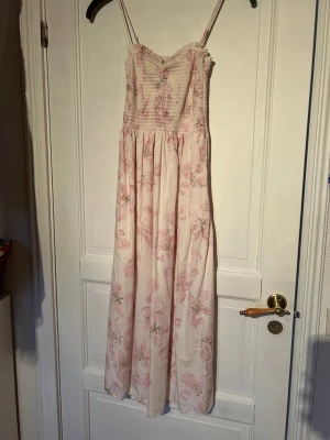 Ljusrosa blommig långklänning - Säljer en söt ljusrosa långklänning med blommigt mönster och smala axelband. Klänningen har rynkad överdel och ett luftig nertill. Använd 1 gång, väldigt fint skick! 