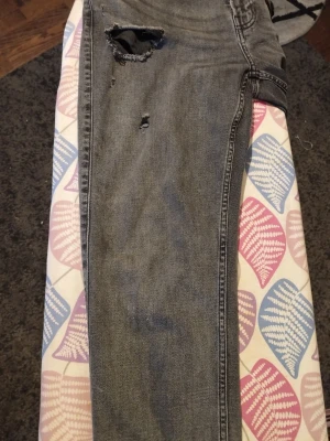 Grå slitna jeans från Hollister - Säljer ett par grå jeans från Hollister med slim straight passform och avancerad stretch. Byxorna har tydliga slitningar och hål på benen för en edgy look. Klassisk femficksdesign och knappgylf. Perfekt för dig som gillar streetstyle.
