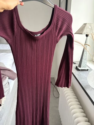 Vinröd ribbad långklänning H&M - Säljer en vinröd långklänning från H&M i storlek S. Klänningen är ribbad med långärmade, lätt utsvängda ärmar och har en rundad halsringning. Materialet är mjukt och stretchigt, perfekt för dig som gillar en slim passform och stilren look.